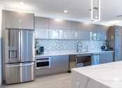 Thumbnail 17 of 22 - A modern kitchen with a stainless steel refrigerator and a white countertop.