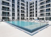 Thumbnail 12 of 26 - A large swimming pool in front of a building with white balconies.