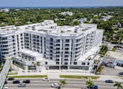Thumbnail 1 of 26 - A large white building with a green roof is surrounded by a parking lot.