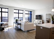 Thumbnail 17 of 52 - A modern living room with a white couch, a wooden cabinet, and a large window overlooking the city.