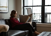 Thumbnail 15 of 52 - A woman in a red sweater is sitting on a black leather couch at The Pearl, Fort Wayne, 46802