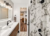Thumbnail 6 of 10 - A bathroom with a marble tile shower and a wooden vanity.