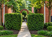 Thumbnail 4 of 10 - A pathway leads through a garden with green bushes and trees.