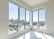 Thumbnail 52 of 88 - A sunny room with large windows overlooking a cityscape and beach.