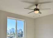 Thumbnail 16 of 88 - A room with a ceiling fan and a large window overlooking a cityscape.
