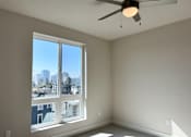 Thumbnail 22 of 88 - A room with a ceiling fan and a window overlooking a cityscape.