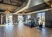 Thumbnail 7 of 8 - a gym with fitness equipment and windows in a building with wood floors