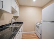 Thumbnail 17 of 20 - A kitchen with a white refrigerator, sink, and cabinets.