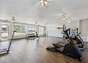 Thumbnail 20 of 42 - A gym with treadmills, elliptical machines, and a fan.