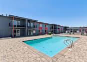 Thumbnail 35 of 42 - A swimming pool surrounded by a brick patio and apartment buildings.