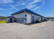 Thumbnail 14 of 29 - a white building with a blue roof and a parking lot with cars
