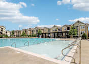 Thumbnail 43 of 60 - A large swimming pool with a concrete edge and metal handrails is surrounded by apartment buildings at Venue at 109 Apartments, Tennessee