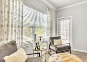 Thumbnail 3 of 39 - A living room with a grey couch, a chair, a small table with a vase and a picture frame on it, and a window with white blinds.