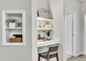 Thumbnail 9 of 39 - A white desk with a chair and a shelf with a plant and other decorations.
