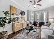Thumbnail 1 of 41 - A living room with a ceiling fan, a large painting, a wooden cabinet, a coffee table, and a potted plant.