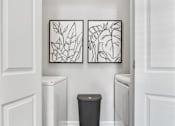 Thumbnail 8 of 41 - A hallway with a trash can and two framed pictures on the wall.