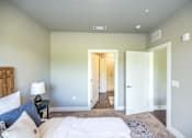 Thumbnail 7 of 20 - A bedroom with a bed, nightstand, and a doorway leading to another room.
