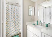 Thumbnail 18 of 28 - A bathroom with a checkered shower curtain and white cabinets.