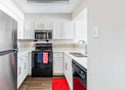 Thumbnail 9 of 28 - A kitchen with white cabinets and a red rug on the floor.
