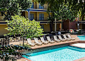 Thumbnail 25 of 28 - A pool surrounded by chairs and trees in front of a building.