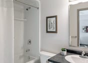 Thumbnail 13 of 15 - A bathroom with a white tub, sink, and a picture on the wall.