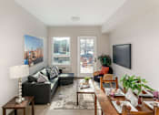 Thumbnail 6 of 15 - A living room with a black couch, a wooden coffee table, and a large window.
