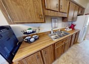 Thumbnail 5 of 21 - A kitchen with wooden cabinets and a black fridge.