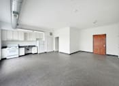 Thumbnail 7 of 22 - A large empty room with a kitchen area to the left.