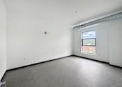 Thumbnail 4 of 22 - A large empty room with a window and a fire extinguisher on the wall.