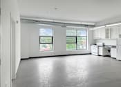 Thumbnail 3 of 22 - A large empty room with a kitchenette and two windows.