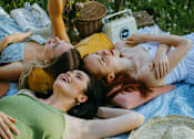 Thumbnail 12 of 22 - Three people are lying on a blanket in a field.