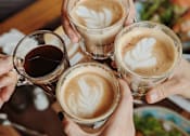 Thumbnail 7 of 22 - Four hands holding glasses of coffee with latte art.