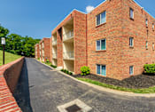 Thumbnail 62 of 65 - Side view of a brick apartment building with balconies and paved drive at Aspen Village
