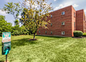Thumbnail 65 of 65 - Open green lawn with pet waste station beside a brick apartment building at Aspen Village