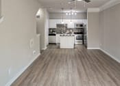 Thumbnail 2 of 61 - Open living room and kitchen with wood-look flooring, breakfast bar, and pendant lighting in a one-bedroom apartment at The Brownstones in Far North Dallas