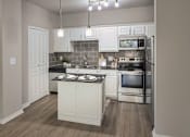 Thumbnail 1 of 61 - Kitchen with white cabinets, stainless steel appliances, tile backsplash, and center island in a one-bedroom apartment at The Brownstones