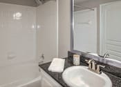 Thumbnail 7 of 61 - Bathroom with tub-shower combination, white vanity, and dark countertop at The Brownstones in Dallas