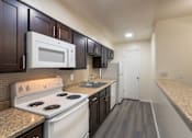 Thumbnail 18 of 62 - A kitchen with dark wood cabinets and white appliances in a 1 bedroom, 1 bath C, 653 sq ft apartment home with hardwoodlike flooring throughout at The Biltmore Apartments located in the Vickery Midtown neighborhood of Dallas, TX.