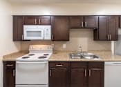 Thumbnail 19 of 62 - A kitchen with dark wood cabinets and white appliances in a 1 bedroom, 1 bath C, 653 sq ft apartment home with hardwoodlike flooring throughout at The Biltmore Apartments located in the Vickery Midtown neighborhood of Dallas, TX.