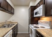 Thumbnail 22 of 62 - A kitchen with dark wood cabinets and white appliances in a 1 bedroom, 1 bath B, 629 sq ft apartment home at The Biltmore Apartments located in the Vickery Midtown neighborhood of Dallas, TX.