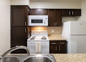 Thumbnail 23 of 62 - A kitchen with dark wood cabinets and white appliances in a 1 bedroom, 1 bath B, 629 sq ft apartment home at The Biltmore Apartments located in the Vickery Midtown neighborhood of Dallas, TX.