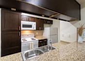 Thumbnail 21 of 62 - A kitchen with dark wood cabinets and white appliances in a 1 bedroom, 1 bath B, 629 sq ft apartment home at The Biltmore Apartments located in the Vickery Midtown neighborhood of Dallas, TX.