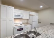 Thumbnail 5 of 62 - A kitchen with white appliances and cabinets with hardwoodlike flooring throughout in a 2 bedroom, 2 bath 991 sq ft apartment home at The Biltmore Apartments located in the Vickery Midtown neighborhood of Dallas, TX.