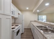 Thumbnail 6 of 62 - A kitchen with white appliances and cabinets with hardwoodlike flooring throughout in a 2 bedroom, 2 bath 991 sq ft apartment home at The Biltmore Apartments located in the Vickery Midtown neighborhood of Dallas, TX.