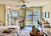 Thumbnail 9 of 47 - Living and sleeping area in an Efficiency apartment at Cambridge Court Apartments in Dallas, Texas, showing carpeted flooring, patio door, dining space, and connection to the kitchen.