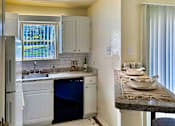 Thumbnail 2 of 47 - Kitchen in an Efficiency apartment at Cambridge Court Apartments in Dallas, Texas, featuring white cabinetry, range, sink, counter space, and a window.