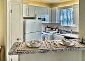 Thumbnail 1 of 47 - Kitchen and breakfast bar in an Efficiency apartment at Cambridge Court Apartments in Dallas, Texas, showing counter space, cabinetry, appliances, and open connection to the living area.