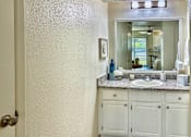 Thumbnail 15 of 47 - Bathroom vanity in an Efficiency apartment at Cambridge Court Apartments in Dallas, Texas, featuring white cabinetry, mirror, sink, and counter space.