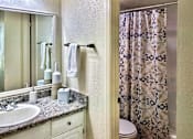 Thumbnail 14 of 47 - Bathroom vanity and tub/shower area in an Efficiency apartment at Cambridge Court Apartments in Dallas, Texas, featuring counter space, mirror, and shower curtain.