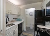 Thumbnail 4 of 47 - Kitchen in a 1-bedroom apartment at Cambridge Court Apartments in Dallas, Texas, featuring white cabinetry, black appliances, sink, and counter space.